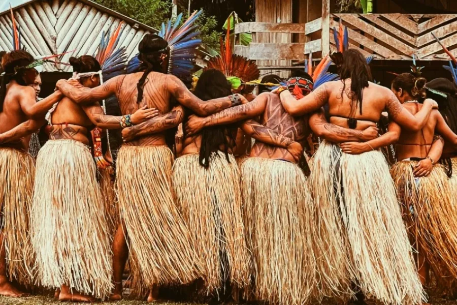 Un gruppo di persone del popolo Shanenawa in cerchio, con pitture corporali tradizionali, copricapi di piume colorate e gonne di paglia, che celebrano un rituale ancestrale nel villaggio, nel cuore dell'Amazzonia.