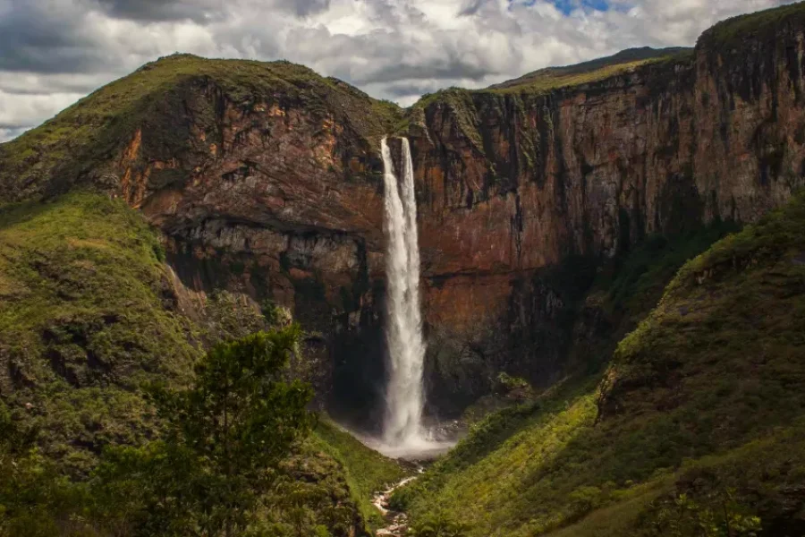 Waterfall cascading down a rocky cliff in Serra do Cipó, surrounded by cerrado vegetation.
