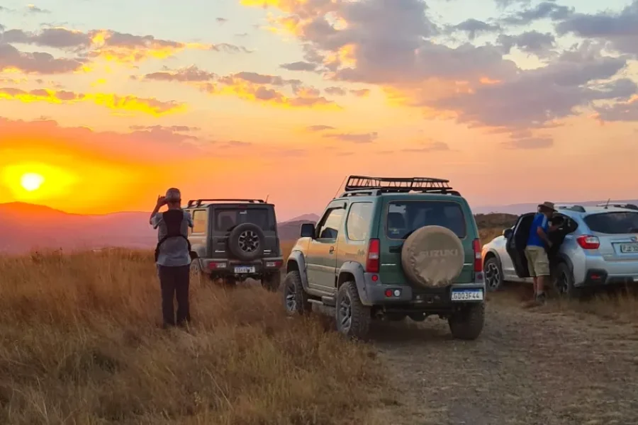Grupo de viajantes e jipes 4x4 num mirante da Serra da Canastra a fotografar o pôr do sol dourado sobre as serras e campos do Cerrado, no Parque Nacional da Serra da Canastra, Minas Gerais, Brasil.
