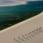 Group of trekkers walking on white sand dunes at Lençóis Maranhenses with emerald lagoon — trekking in Brazil