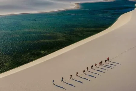 Group of trekkers walking on white sand dunes at Lençóis Maranhenses with emerald lagoon — trekking in Brazil