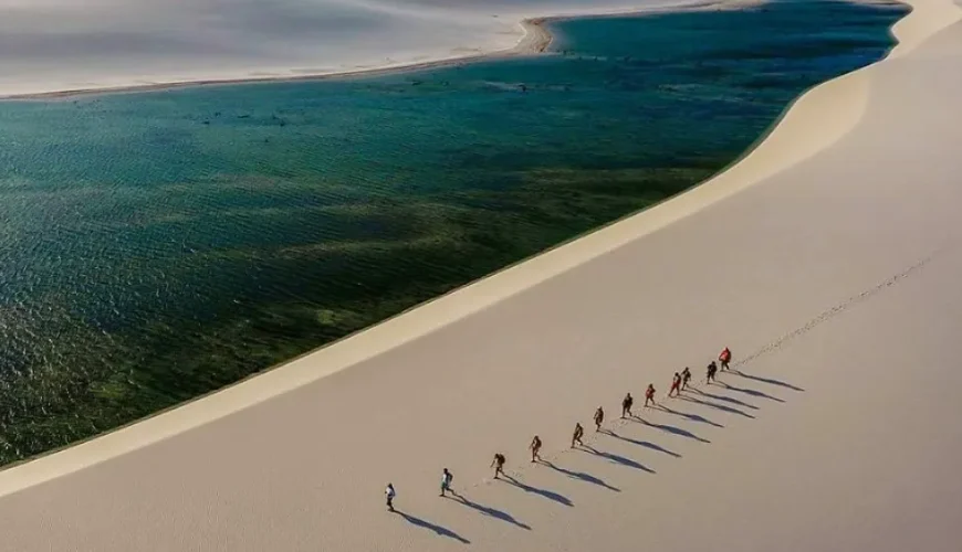 Group of trekkers walking on white sand dunes at Lençóis Maranhenses with emerald lagoon — trekking in Brazil
