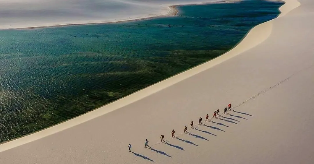 Group of trekkers walking on white sand dunes at Lençóis Maranhenses with emerald lagoon — trekking in Brazil