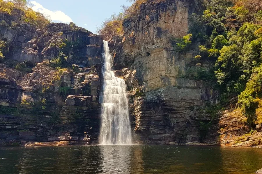 Salto Garimpão precipitándose por un acantilado de roca estratificada con vegetación del Cerrado, formando una piscina natural de aguas tranquilas en la base de la caída, en la Chapada dos Veadeiros, Goiás, Brasil.