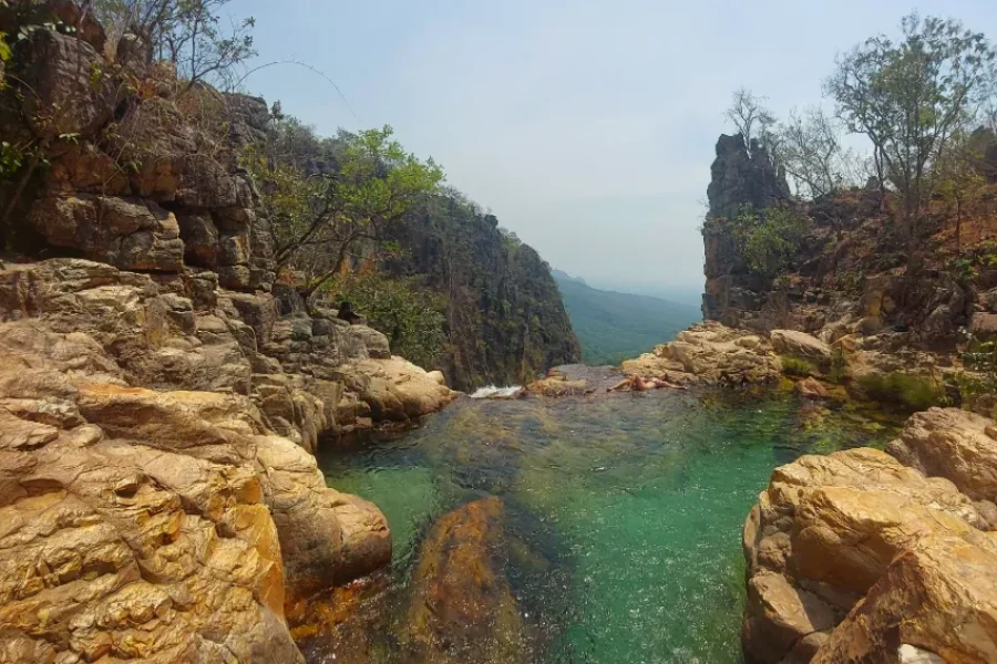Piscina natural de aguas verdosas y cristalinas encajada entre paredes de roca anaranjada y vegetación nativa en el Complexo Águas Lindas, en Cavalcante, Goiás, Brasil.