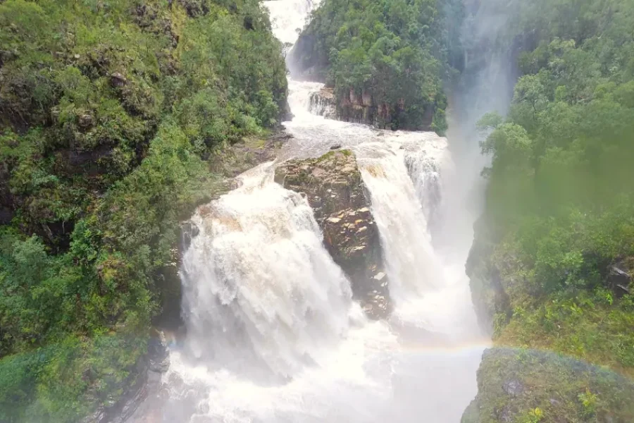 Cataratas dos Couros en plena fuerza, con varias caídas de agua precipitándose entre rocas y densa vegetación del Cerrado, con un arcoíris formándose en la niebla de las aguas, en la Chapada dos Veadeiros, Goiás, Brasil.