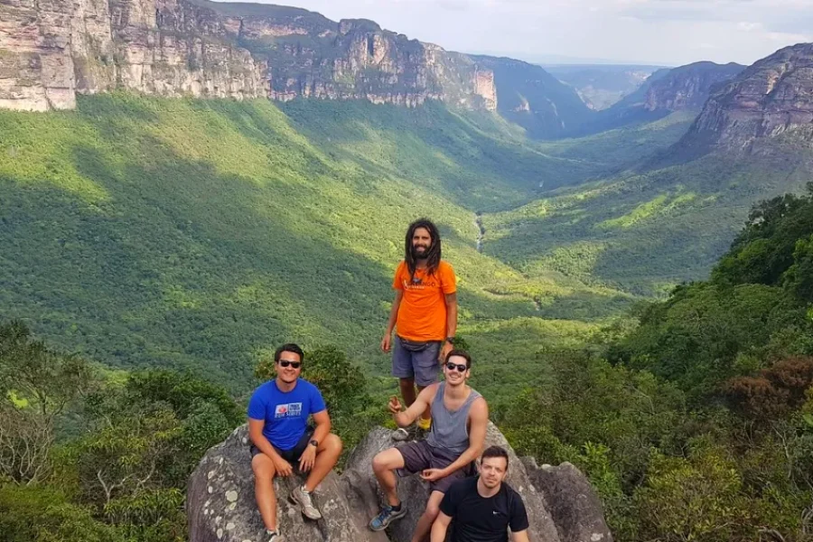 Un groupe de quatre voyageurs posant à un belvédère rocheux avec une vue panoramique sur le Vale do Pati, entouré de parois rocheuses et de forêt verte de la Chapada Diamantina, en Bahia, Brésil.