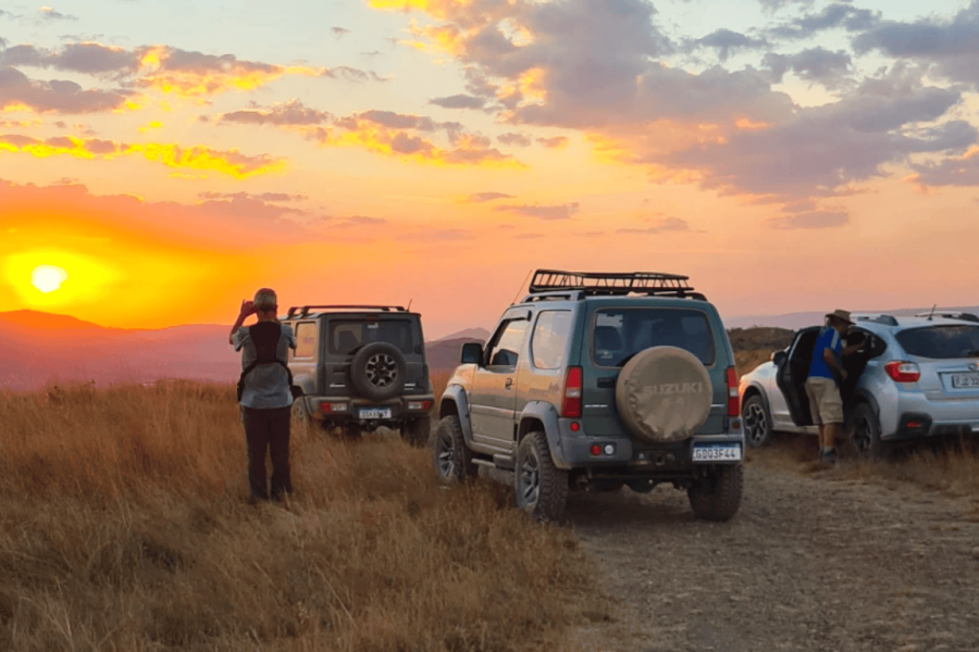 Veículos 4x4 estacionados na Serra da Canastra durante o pôr do sol, com viajantes admirando a paisagem dourada