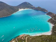 Vista aerea della Praia do Forno ad Arraial do Cabo, con le sue acque turchesi e verde smeraldo, sabbia bianca e barche ancorate nell'insenatura, circondata da colline con vegetazione bassa, nello stato di Rio de Janeiro, Brasile.