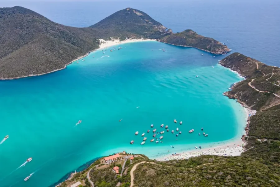 Aerial view of Praia do Forno in Arraial do Cabo, with its turquoise and emerald-green waters, white sand and boats anchored in the cove, surrounded by hills with low-lying vegetation, in Rio de Janeiro, Brazil.