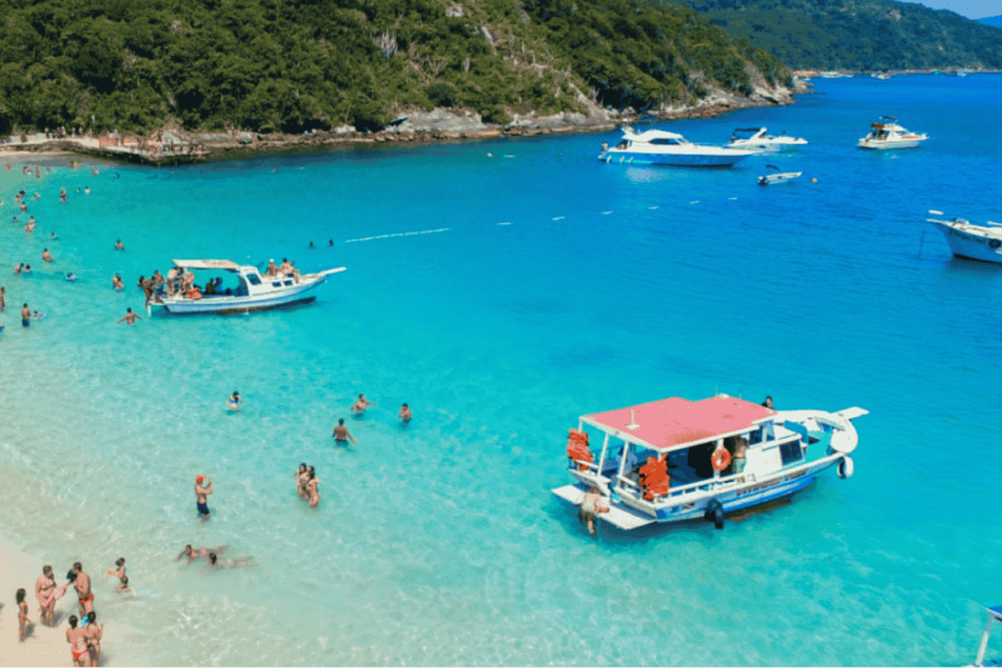 Boat trip in Arraial do Cabo with crystal-clear turquoise waters, anchored boats, and people swimming at a paradise beach.