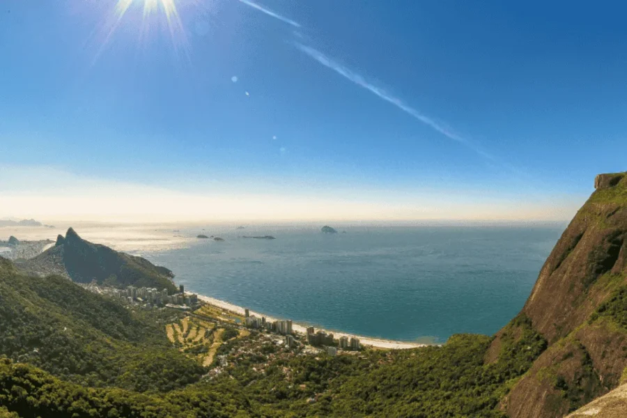 Vista panorámica desde la Pedra Bonita sobre la playa de São Conrado, la Barra da Tijuca, el Morro Dois Irmãos y el océano Atlántico, con el Bosque de Tijuca enmarcando el paisaje bajo un cielo azul, en Río de Janeiro, Brasil.