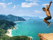 Un viaggiatore che salta in cima alla Pedra do Telégrafo, con una vista mozzafiato sulle spiagge selvagge, le insenature turchesi e la Foresta di Tijuca lungo la costa occidentale di Rio de Janeiro, Brasile.