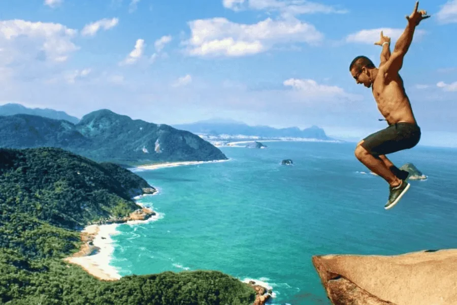 A traveller jumping at the summit of Pedra do Telégrafo, with a breathtaking view over wild beaches, turquoise coves and the Tijuca Forest along the western coast of Rio de Janeiro, Brazil.