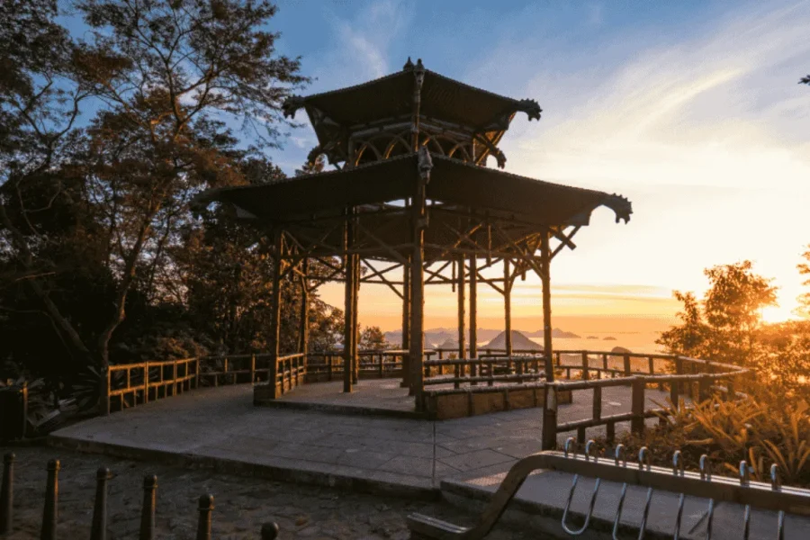 Pabellón de estilo oriental de la Vista Chinesa al atardecer, con su estructura de madera recortada contra el cielo anaranjado y la Bahía de Guanabara al fondo, en el Bosque de Tijuca, Río de Janeiro, Brasil.