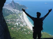 Silhouette di un viaggiatore con le braccia alzate in cima alla Garganta do Céu, con una vista panoramica sulla spiaggia di São Conrado, la Barra da Tijuca e l'oceano Atlantico, a Rio de Janeiro, Brasile.