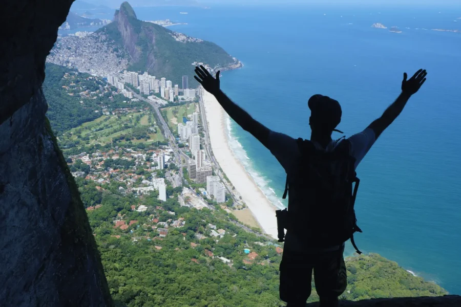 Silhouette of a traveller with arms raised at the summit of Garganta do Céu, with a panoramic view over São Conrado beach, Barra da Tijuca and the Atlantic Ocean, in Rio de Janeiro, Brazil.