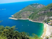 Vista aerea della Praia Vermelha e dell'insenatura del Morro da Urca, con acque turchesi e sabbia dorata circondate da una fitta foresta atlantica e scogliere rocciose, a Rio de Janeiro, Brasile.