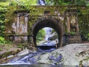 Un arco di pietra storico ricoperto di muschio nella Foresta di Tijuca, con una cascata che scorre al di sotto e una rigogliosa vegetazione di foresta atlantica tutt'intorno, a Rio de Janeiro, Brasile.