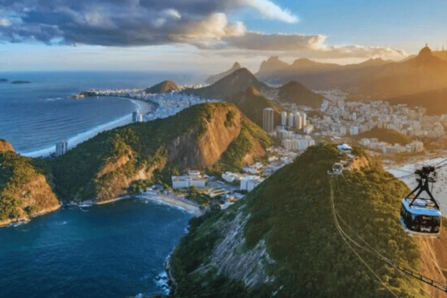 Panoramic view of Rio de Janeiro featuring the iconic Sugarloaf cable car, connecting Morro da Urca to the summit of Sugarloaf Mountain at sunset.