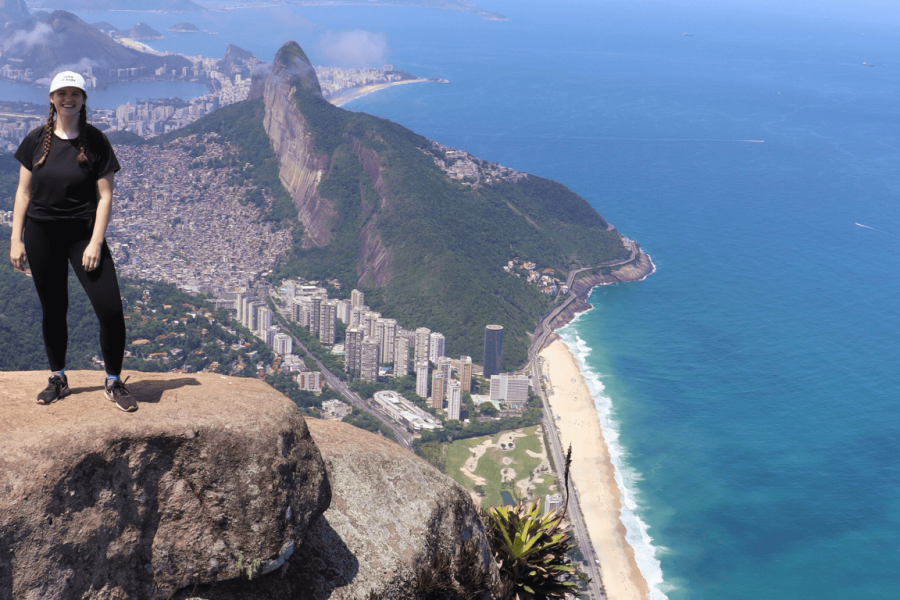 Person at the top of Pedra da Gávea with a panoramic view of Rio de Janeiro’s coastline, including São Conrado Beach and the Rocinha community in the background.
