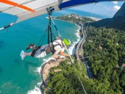 Un viaggiatore in volo in tandem con il deltaplano sulla costa di Rio de Janeiro, con una vista aerea mozzafiato sulle acque turchesi dell'oceano Atlantico, la Foresta di Tijuca e la strada costiera, Brasile.