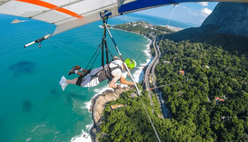 Viajante em voo duplo de asa delta sobre a costa do Rio de Janeiro, com uma vista aérea deslumbrante sobre as águas turquesa do oceano Atlântico, a Floresta da Tijuca e a estrada litorânea, Brasil.