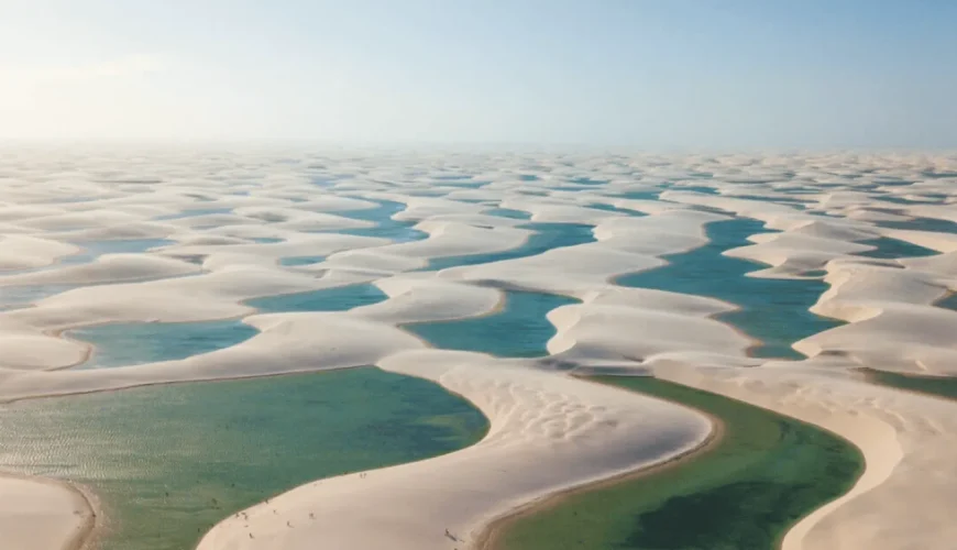 Vista aérea das dunas brancas dos Lençóis Maranhenses com lagoas de águas turquesa e esverdeadas entre as ondulações de areia, no Maranhão, Brasil.