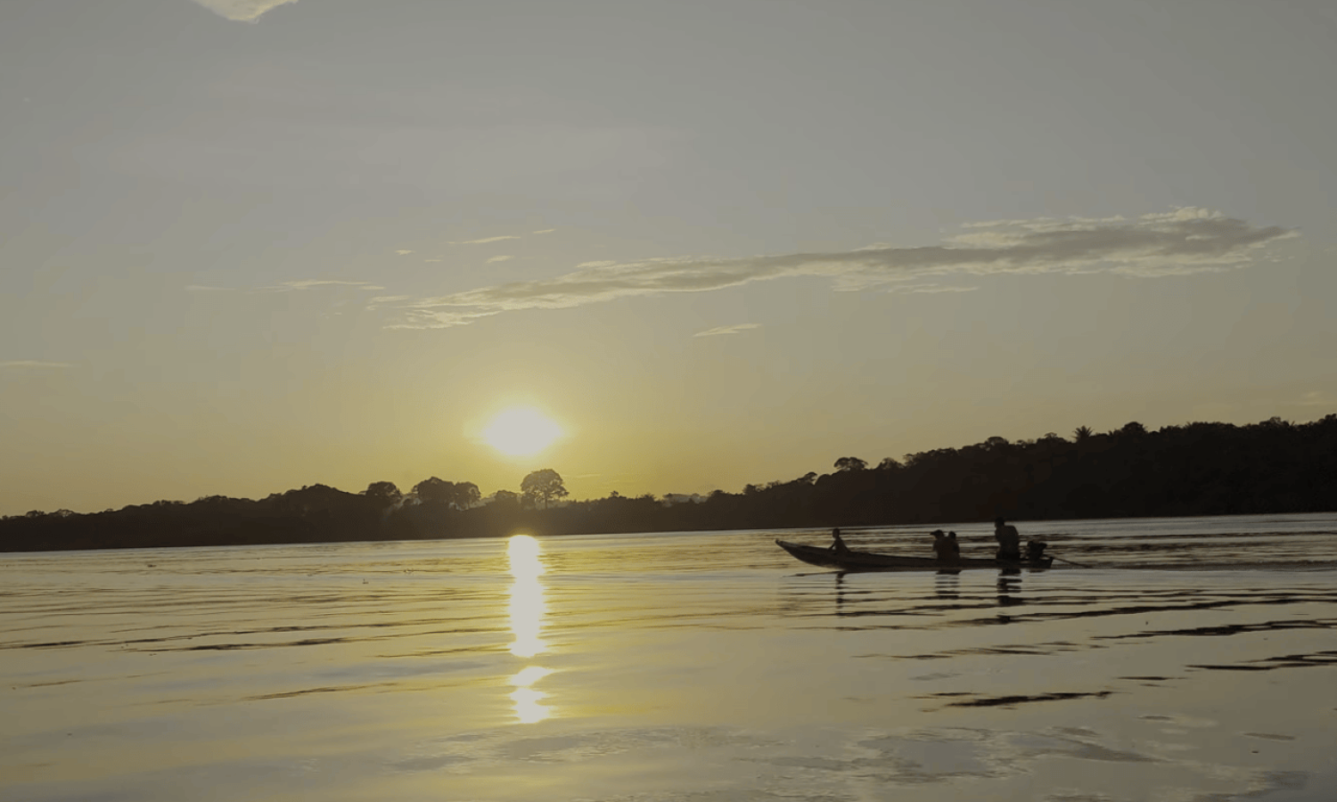 The Rio Negro in Amazonas at sunset, with a wooden boat sailing near the Tiririca community and the golden reflection of the sun shimmering on the calm waters of the Amazon rainforest.