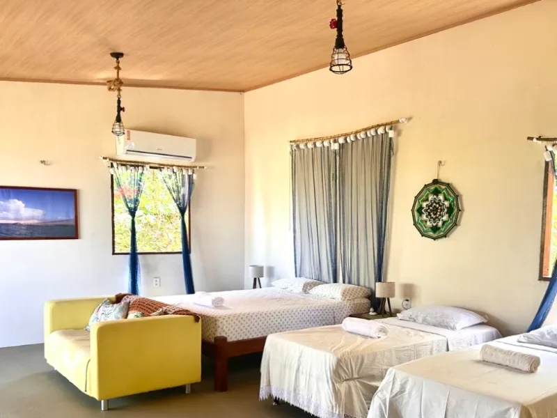 Ingapura Suite at Casa Ingapura — spacious room with double bed, yellow sofa, handcrafted mandala on the wall, air conditioning and window with garden view, Bar da Hora, Lençóis Maranhenses