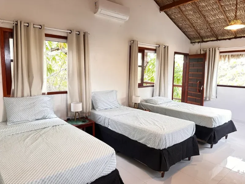 Suite Argonauta im Casa Ingapura — drei Einzelbetten mit heller Bettwäsche, Fenster mit Vorhängen und Naturblick, Strohdach, Bar da Hora, Lençóis Maranhenses