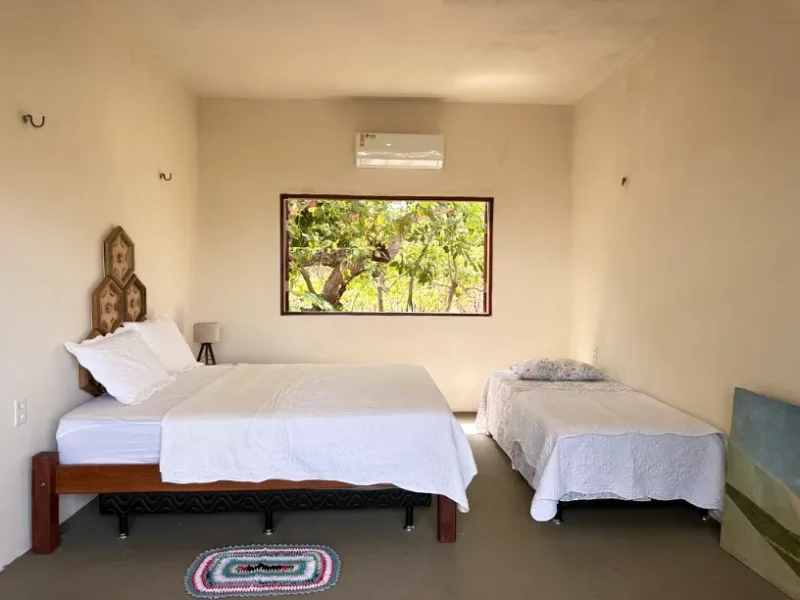 Tainha Suite at Casa Ingapura — double bed and single bed with white linen, handcrafted wooden headboard and window overlooking greenery, Bar da Hora, Lençóis Maranhenses