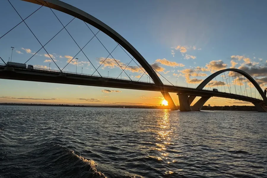 Sun setting between the arches of Ponte JK, seen from the water of Lago Paranoá